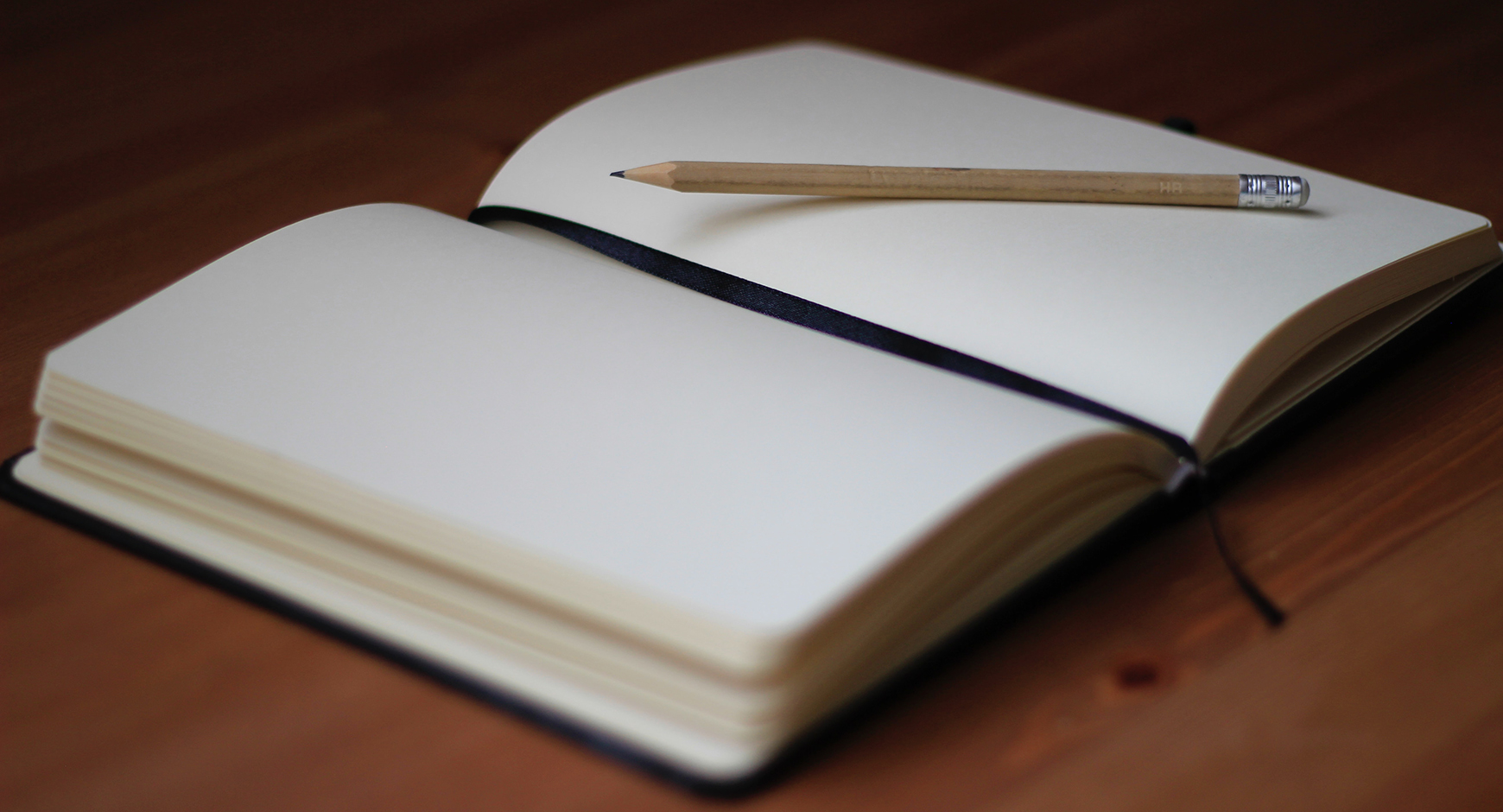 Photo of a journal opened to a blank page with a pencil resting on top. 