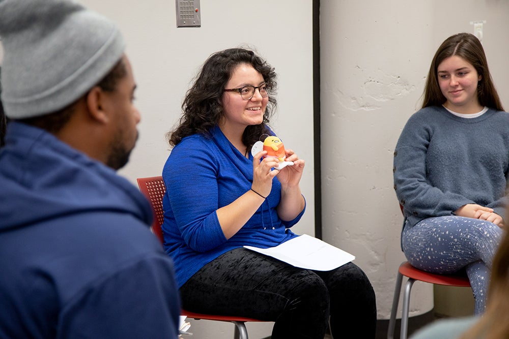 Students sitting in a circle with the woman in focus holding an object