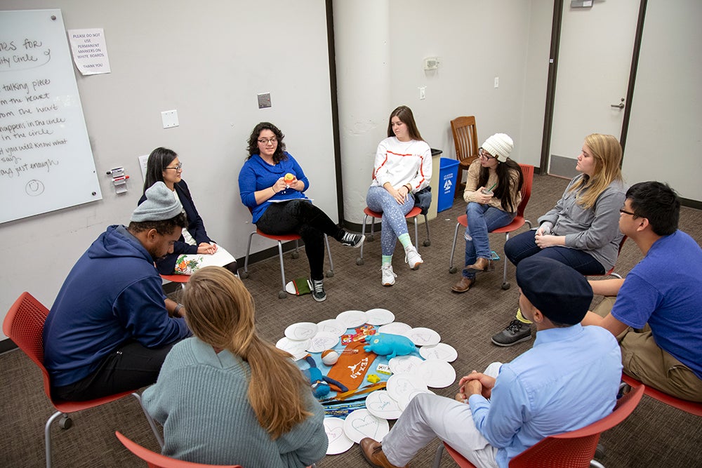 A group of students sitting in a circle around a pile of school supplies