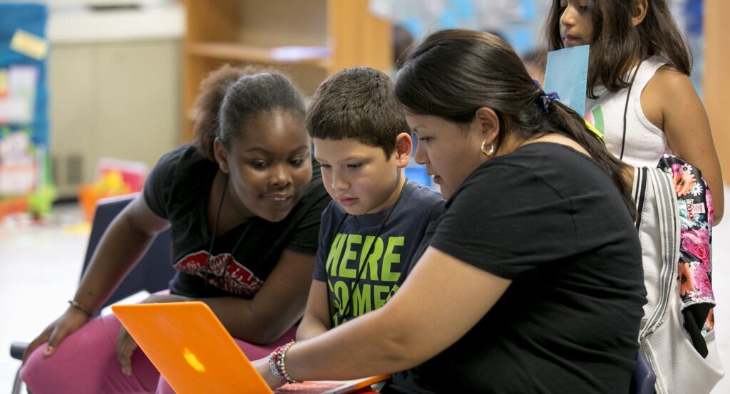 A teacher shows middle school students something on a laptop.