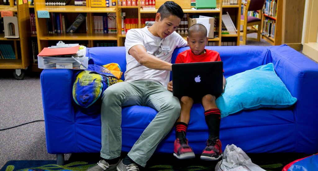 A young man shows a boy how to use a laptop.