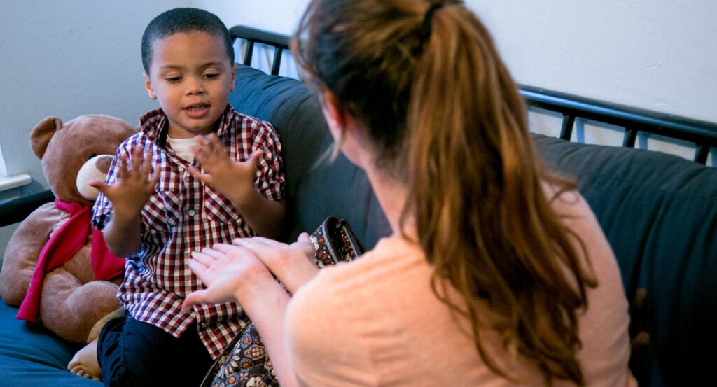 A young woman works with an autistic boy while sitting on a sofa.