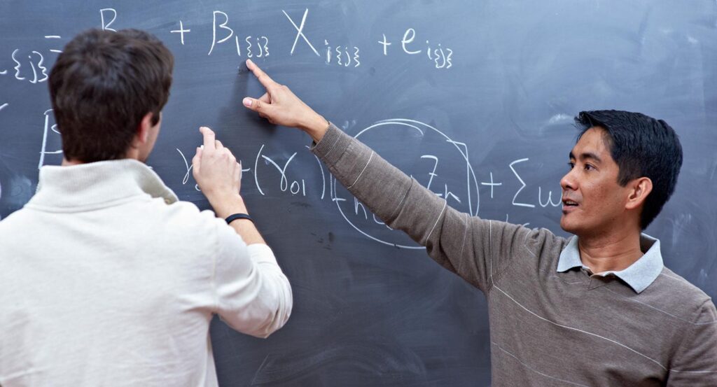 Two young men work on a math problem at a chalkboard.