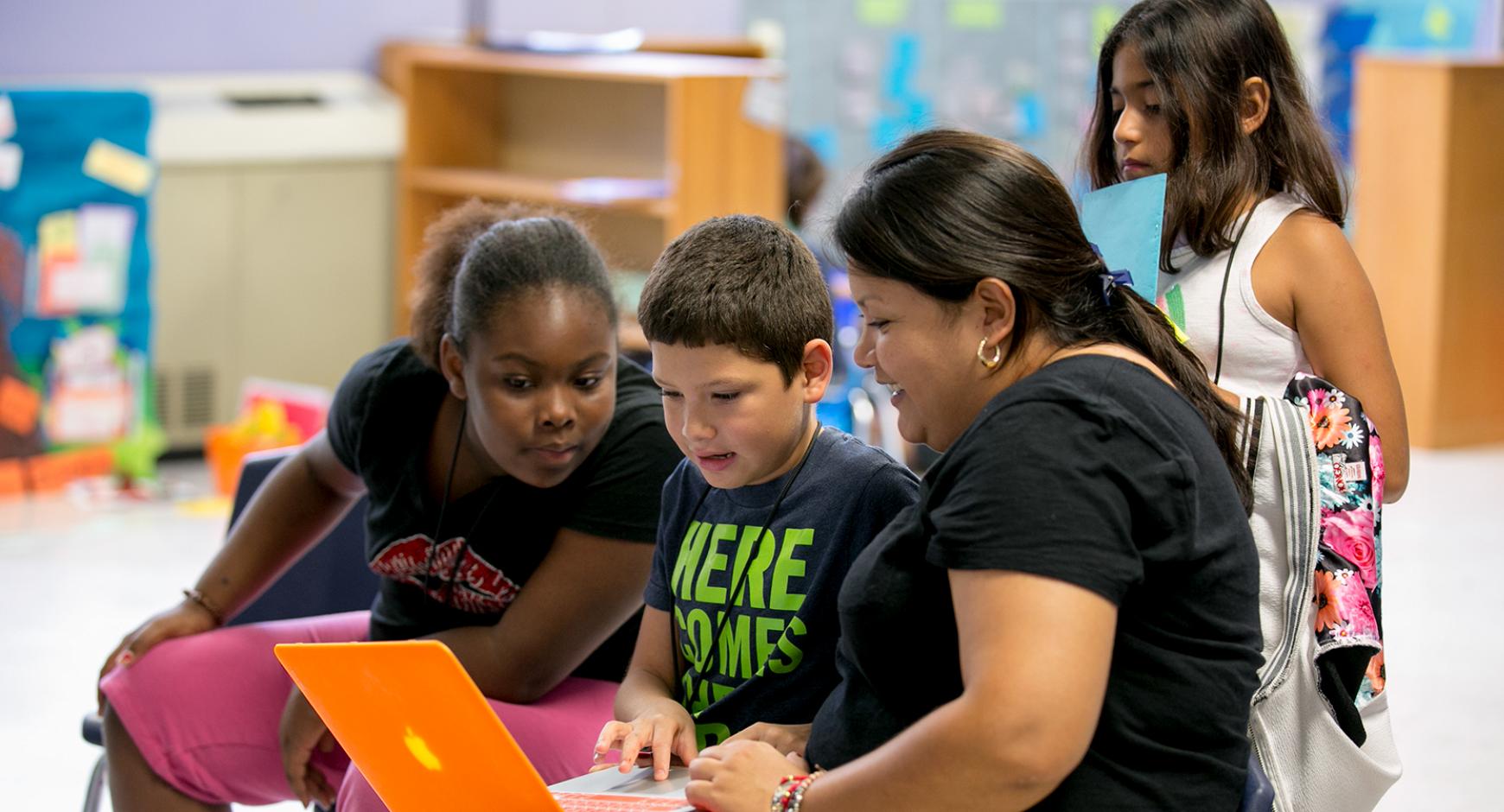 A teacher shares her laptop with her students. 
