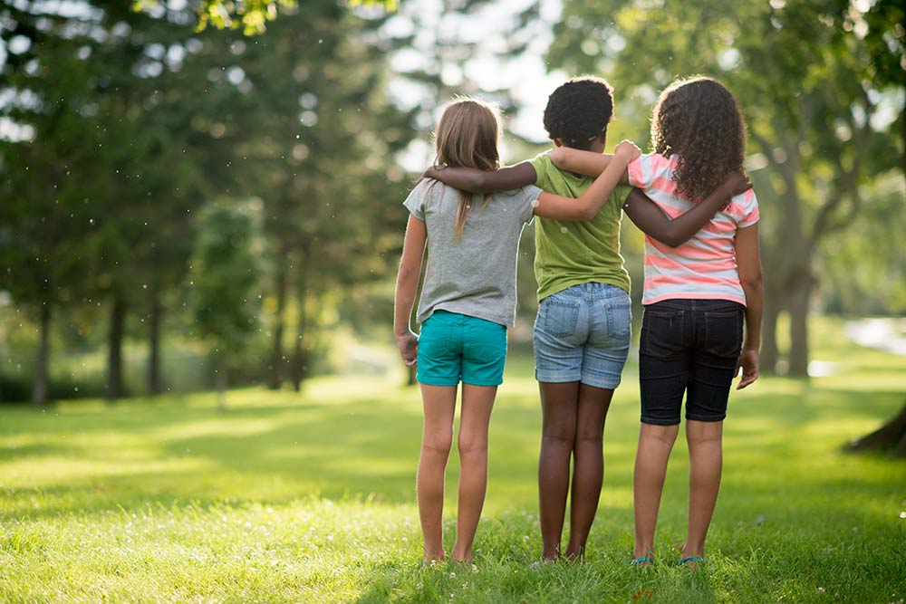 Three children stand with their arms around each other's shoulders