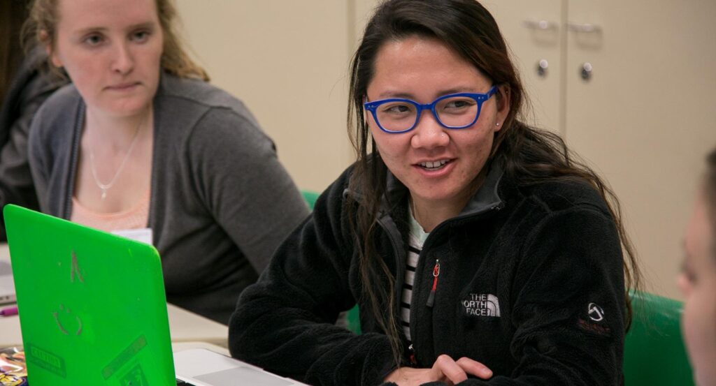 A student looks at her laptop as another woman looks on.