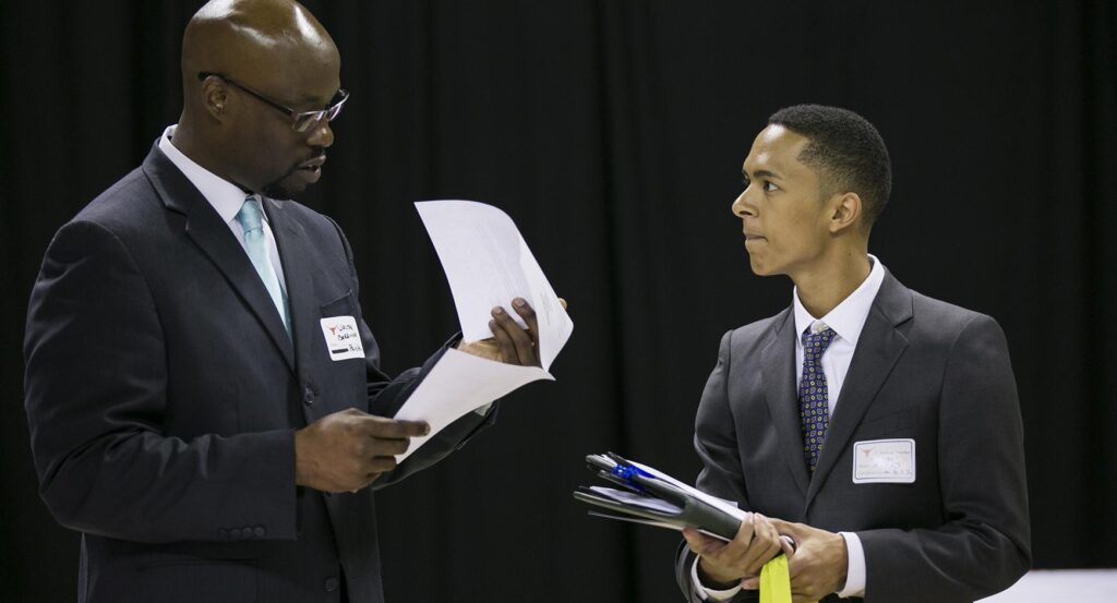 A recruiter looks through a potential applicant's resume at a career fair 
