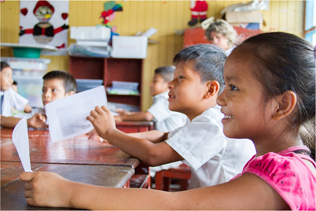 Photo of Peruvian children who are smiling sitting around a table in a classroom.