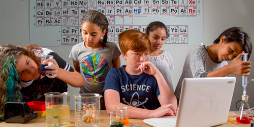 A group of middle school children work at science classroom lab table. 