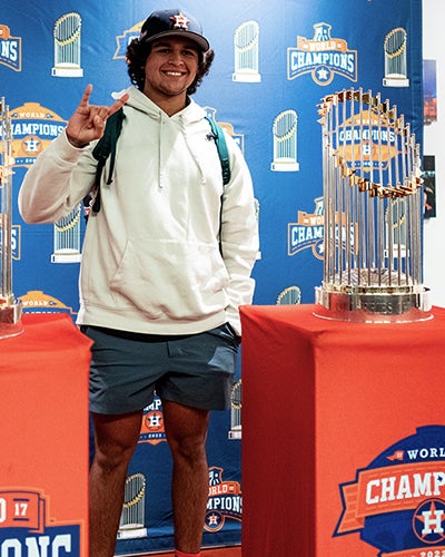 Student poses with Astros world series trophies.